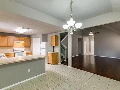 kitchen featuring light wood-type flooring, ceiling fan with notable chandelier, white appliances, kitchen peninsula, and lofted ceiling