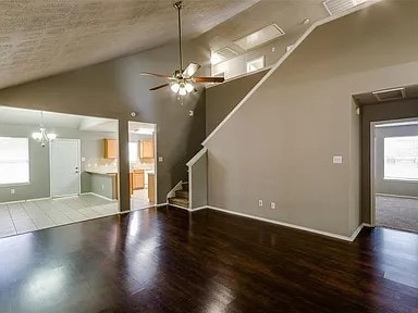 unfurnished living room with ceiling fan with notable chandelier, high vaulted ceiling, and hardwood / wood-style floors