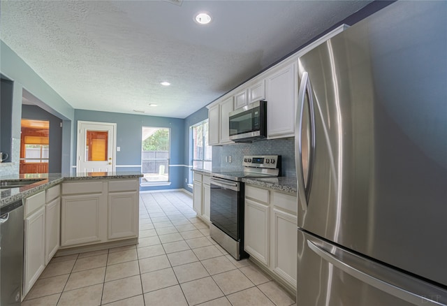 kitchen with appliances with stainless steel finishes, white cabinets, light stone counters, and backsplash