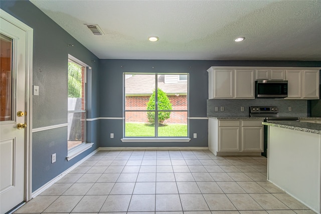 kitchen with a textured ceiling, tasteful backsplash, stainless steel appliances, and light tile patterned floors