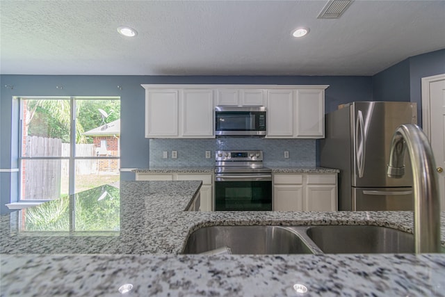 kitchen with decorative backsplash, white cabinets, light stone countertops, and stainless steel appliances