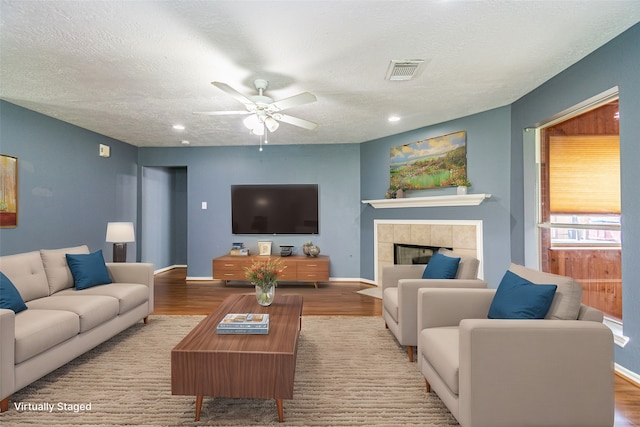 living room featuring light hardwood / wood-style floors, a textured ceiling, a tile fireplace, and ceiling fan