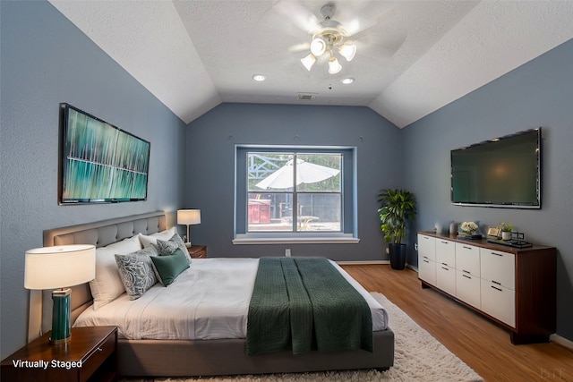 bedroom featuring lofted ceiling, a textured ceiling, light wood-type flooring, and ceiling fan