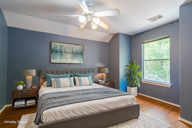 bedroom with a textured ceiling, vaulted ceiling, hardwood / wood-style flooring, and ceiling fan