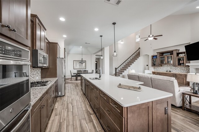 kitchen with light wood-type flooring, stainless steel appliances, sink, a center island with sink, and tasteful backsplash