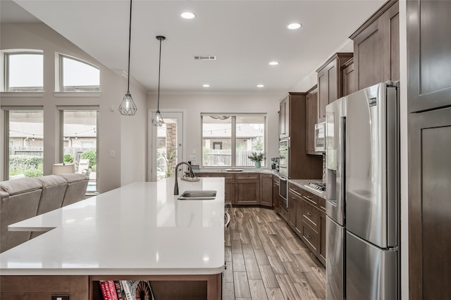 kitchen featuring stainless steel appliances, sink, hanging light fixtures, a center island with sink, and light hardwood / wood-style floors