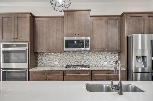 kitchen with backsplash, stainless steel appliances, ornamental molding, sink, and light stone counters