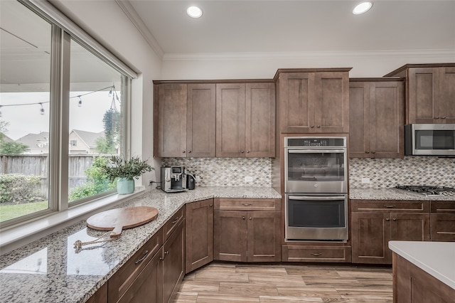 kitchen featuring crown molding, light stone countertops, appliances with stainless steel finishes, and decorative backsplash