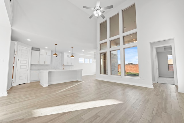 unfurnished living room with ceiling fan, a towering ceiling, and light hardwood / wood-style flooring