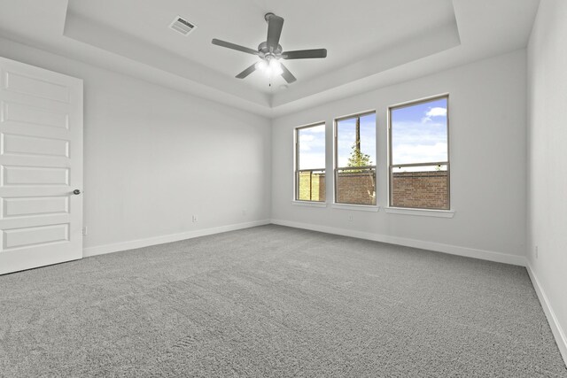 carpeted empty room with ceiling fan and a raised ceiling