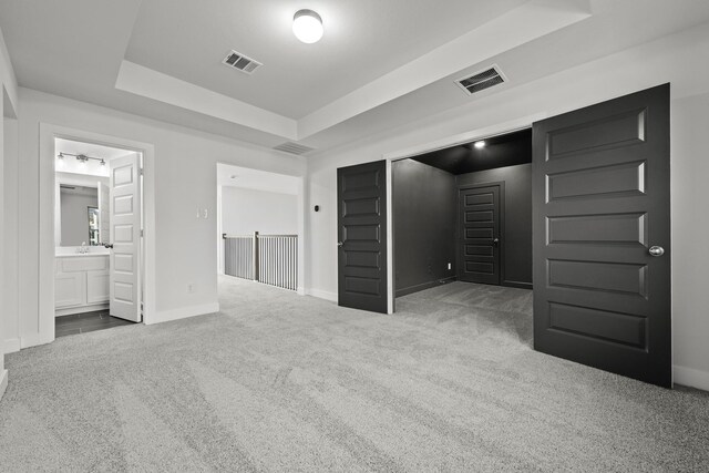 unfurnished bedroom with carpet floors, a raised ceiling, and ensuite bathroom