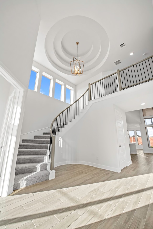 stairs featuring hardwood / wood-style flooring, a notable chandelier, a tray ceiling, and a towering ceiling