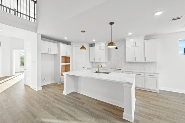 kitchen with light wood-type flooring, light stone countertops, a kitchen island with sink, white cabinets, and sink