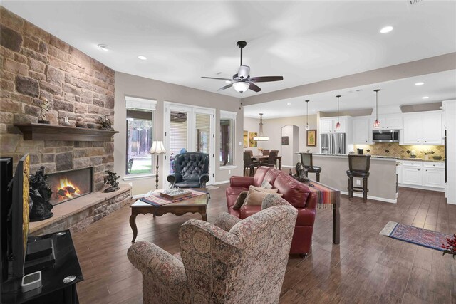 living room featuring dark hardwood / wood-style flooring, ceiling fan, and a stone fireplace