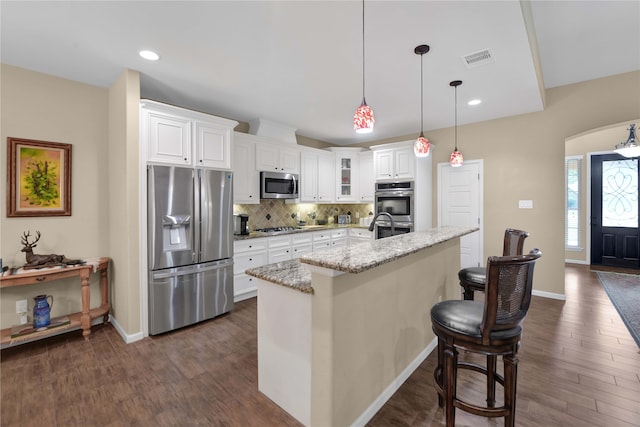 kitchen featuring dark wood-type flooring, stainless steel appliances, light stone counters, and a kitchen island with sink