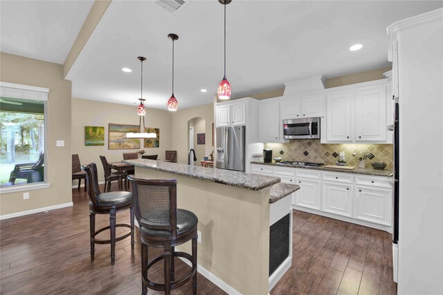 kitchen with a kitchen island with sink, white cabinetry, decorative light fixtures, light stone counters, and appliances with stainless steel finishes