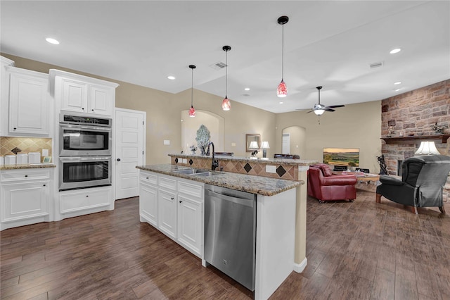 kitchen with a fireplace, a center island with sink, stainless steel appliances, sink, and ceiling fan