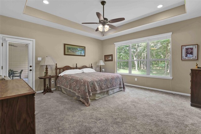 carpeted bedroom featuring a raised ceiling, ceiling fan, and access to outside