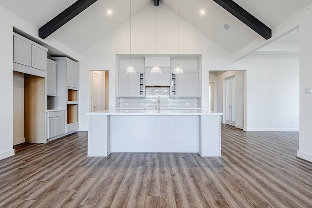 kitchen with decorative light fixtures, beamed ceiling, an island with sink, and high vaulted ceiling