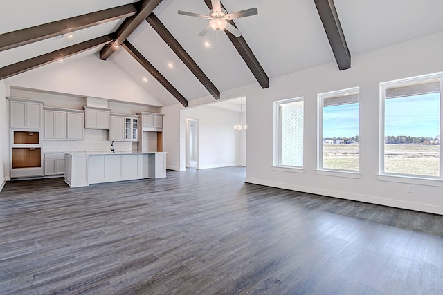 unfurnished living room with ceiling fan with notable chandelier, dark hardwood / wood-style flooring, beamed ceiling, sink, and high vaulted ceiling