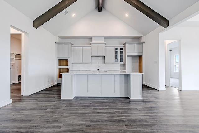 kitchen featuring decorative backsplash, beamed ceiling, light stone countertops, an island with sink, and white cabinets