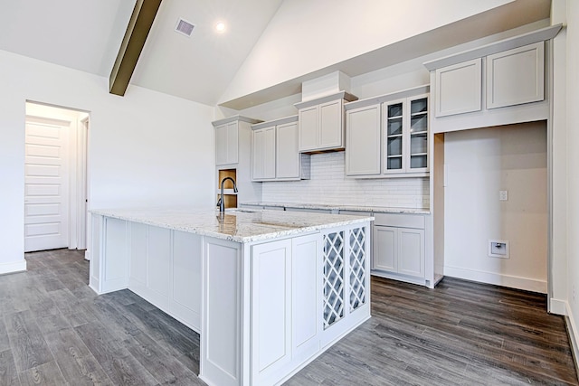 kitchen with tasteful backsplash, sink, a kitchen island with sink, light stone counters, and beam ceiling