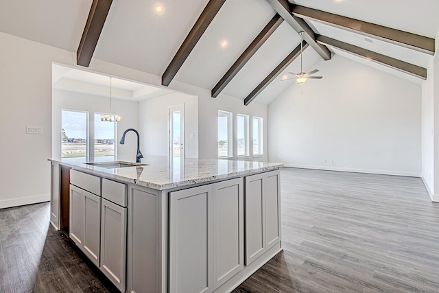 kitchen featuring ceiling fan with notable chandelier, light stone countertops, sink, gray cabinets, and a kitchen island with sink