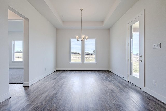 unfurnished dining area featuring dark wood-type flooring, plenty of natural light, a raised ceiling, and an inviting chandelier