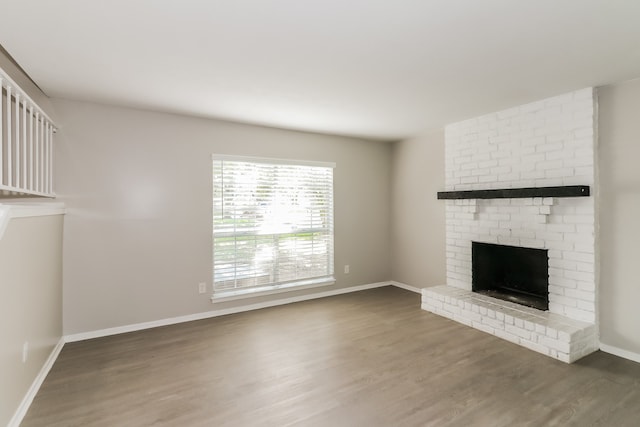 unfurnished living room featuring dark wood-type flooring, brick wall, and a brick fireplace