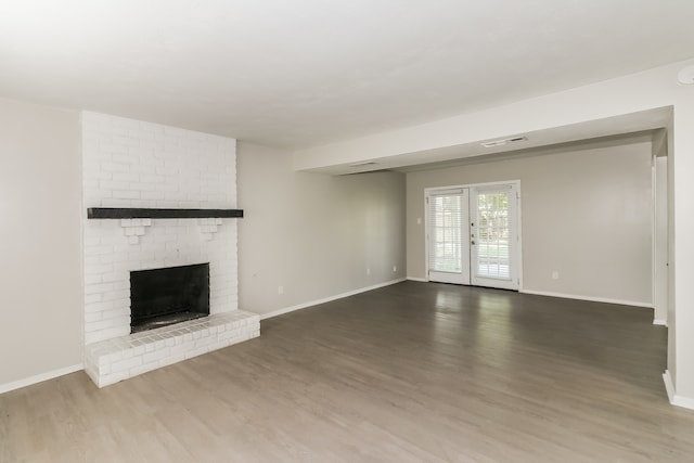 unfurnished living room with brick wall, hardwood / wood-style floors, a brick fireplace, and french doors