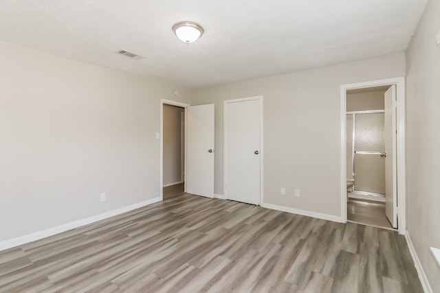 unfurnished bedroom featuring wood-type flooring, ensuite bathroom, and a closet