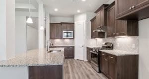 kitchen with light hardwood / wood-style flooring, appliances with stainless steel finishes, light stone counters, dark brown cabinets, and decorative backsplash