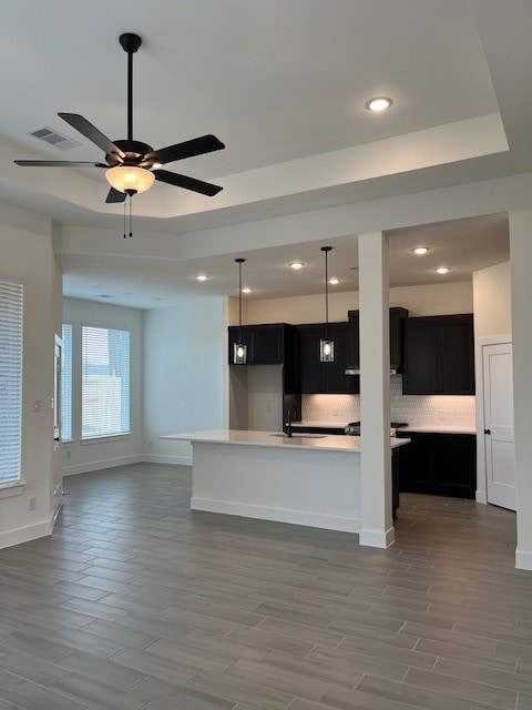 kitchen featuring tasteful backsplash, a kitchen island with sink, light hardwood / wood-style flooring, and a tray ceiling