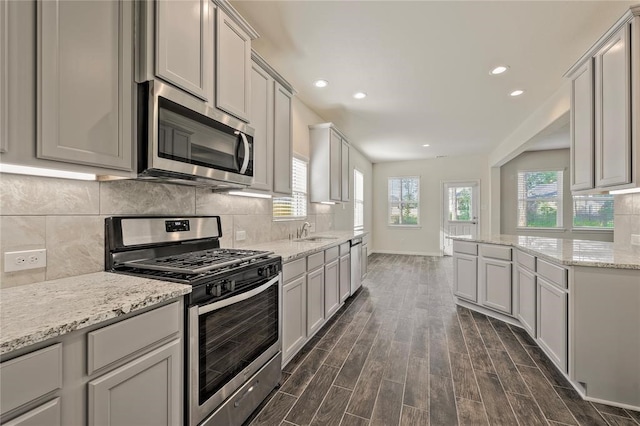 kitchen featuring appliances with stainless steel finishes, light stone countertops, sink, dark wood-type flooring, and tasteful backsplash