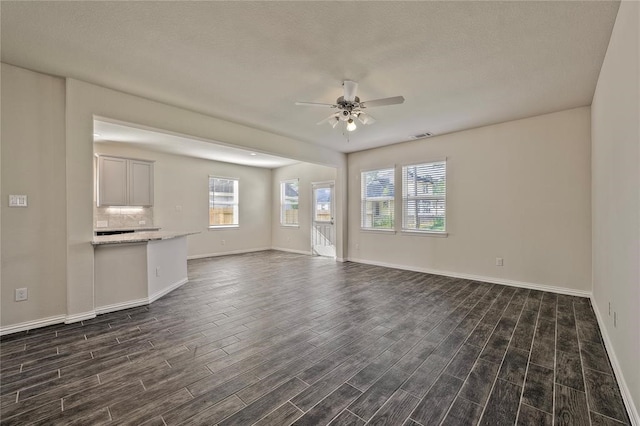 unfurnished living room featuring dark wood-type flooring and ceiling fan