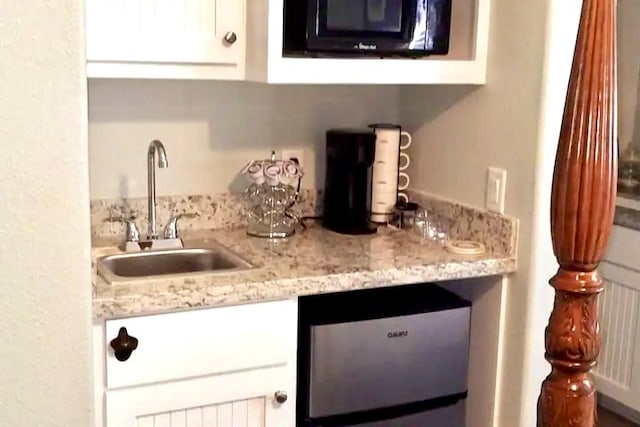 bar featuring stainless steel dishwasher, light stone countertops, white cabinetry, and sink