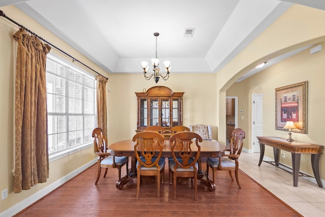 dining space with a raised ceiling, hardwood / wood-style floors, and a notable chandelier