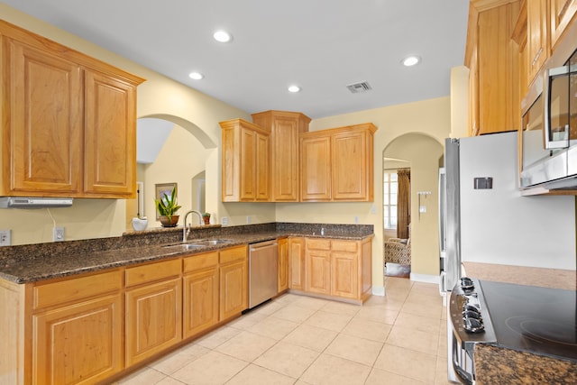 kitchen featuring sink, light tile patterned floors, appliances with stainless steel finishes, and dark stone counters