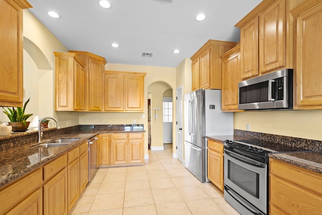 kitchen featuring stainless steel appliances, sink, dark stone countertops, and light tile patterned flooring