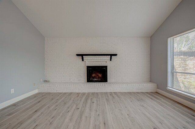 unfurnished living room with vaulted ceiling, light hardwood / wood-style flooring, brick wall, and a brick fireplace