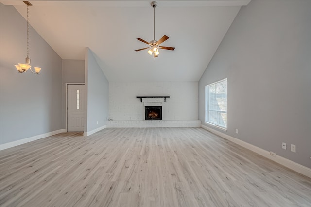 unfurnished living room featuring high vaulted ceiling, ceiling fan with notable chandelier, a fireplace, and light hardwood / wood-style floors