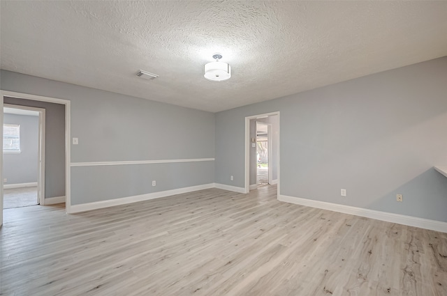 empty room with a textured ceiling, a healthy amount of sunlight, and light wood-type flooring