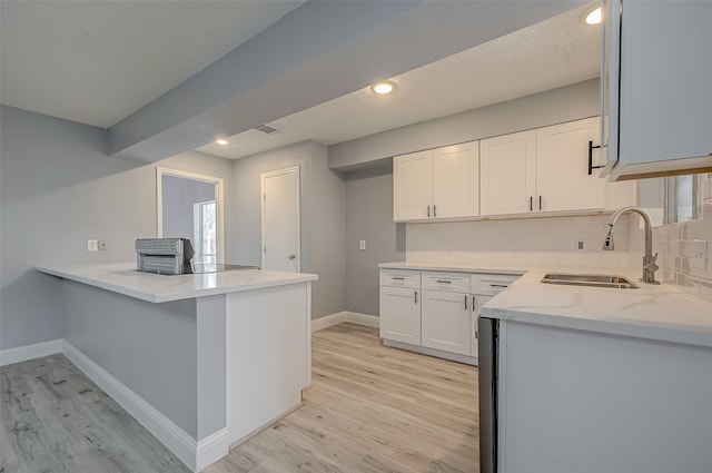 kitchen featuring tasteful backsplash, kitchen peninsula, sink, light wood-type flooring, and white cabinets