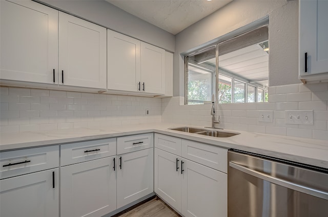 kitchen featuring tasteful backsplash, stainless steel dishwasher, sink, white cabinetry, and light stone counters