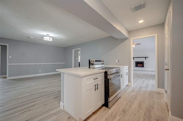 kitchen with a textured ceiling, stainless steel electric stove, a fireplace, light hardwood / wood-style flooring, and white cabinets