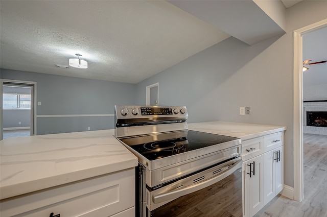 kitchen with stainless steel electric range oven, light wood-type flooring, white cabinetry, and a brick fireplace