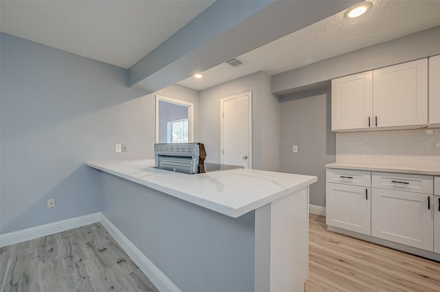 kitchen with light wood-type flooring, white cabinetry, backsplash, light stone counters, and kitchen peninsula