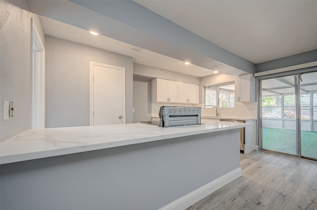 kitchen with white cabinetry, backsplash, light stone counters, kitchen peninsula, and light hardwood / wood-style floors