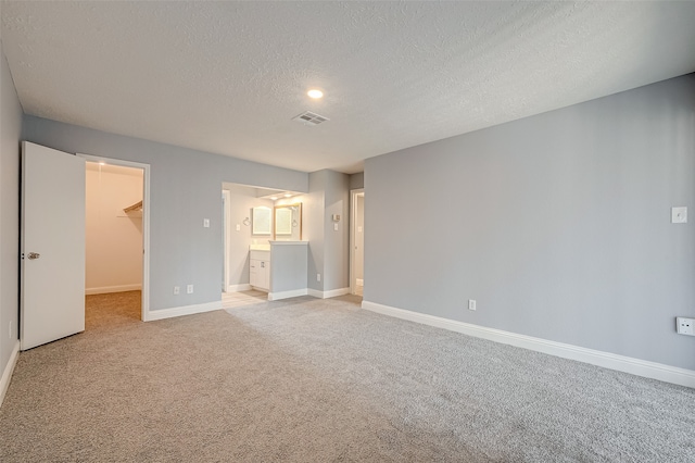 unfurnished bedroom with a walk in closet, ensuite bathroom, light colored carpet, and a closet