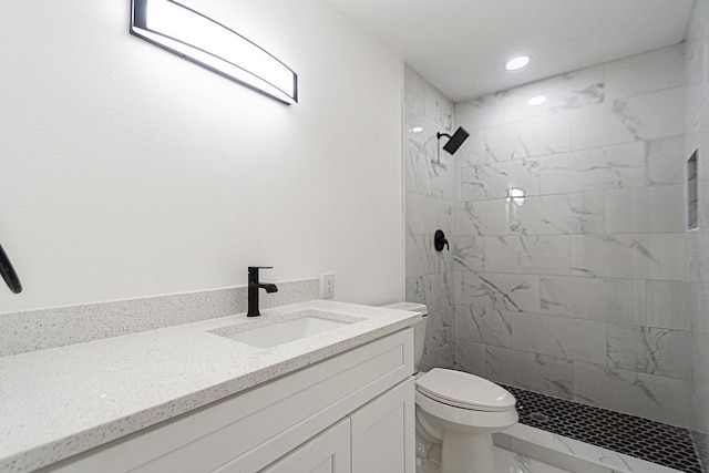 bathroom with toilet, a tile shower, and vanity